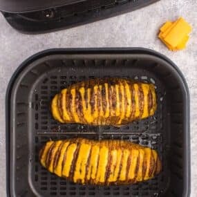Two cooked hasselback potatoes in an air fryer basket with the cheese melted.