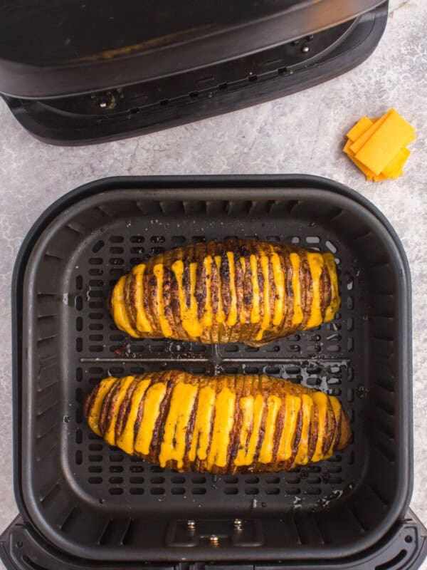 Two cooked hasselback potatoes in an air fryer basket with the cheese melted.