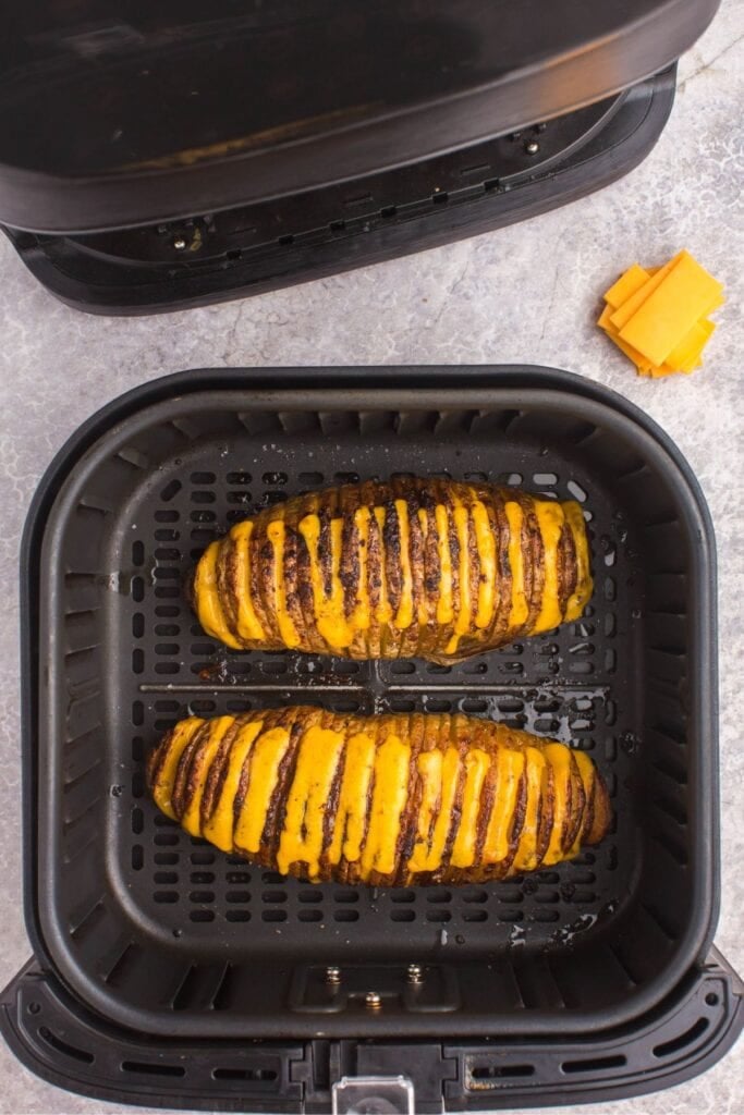 Two cooked hasselback potatoes in an air fryer basket with the cheese melted.