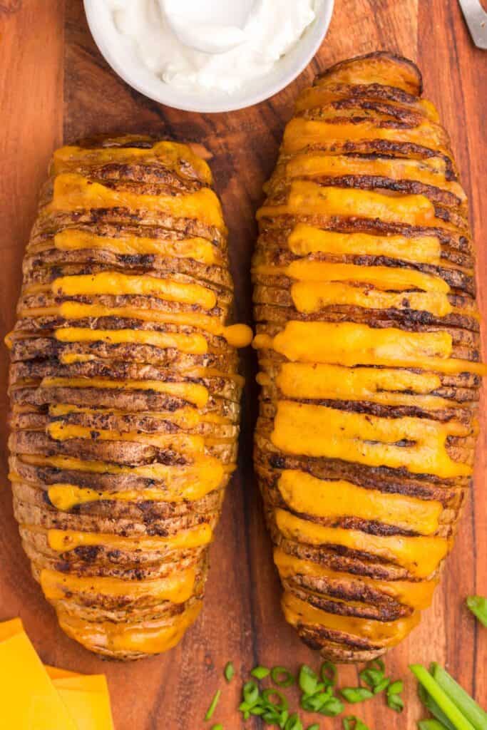 Close up of two air fryer hasselback potatoes on a cutting board.