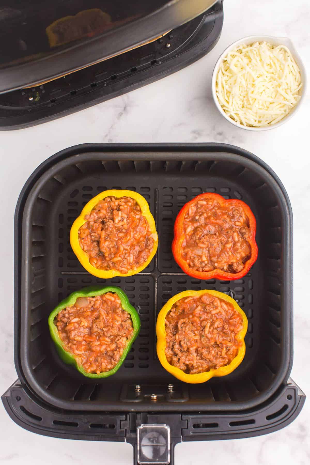 Ground beef mixture in the stuffed peppers inside an air fryer basket.