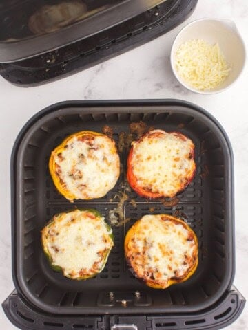 Cooked stuffed peppers in an air fryer basket with browned melted cheese on top.