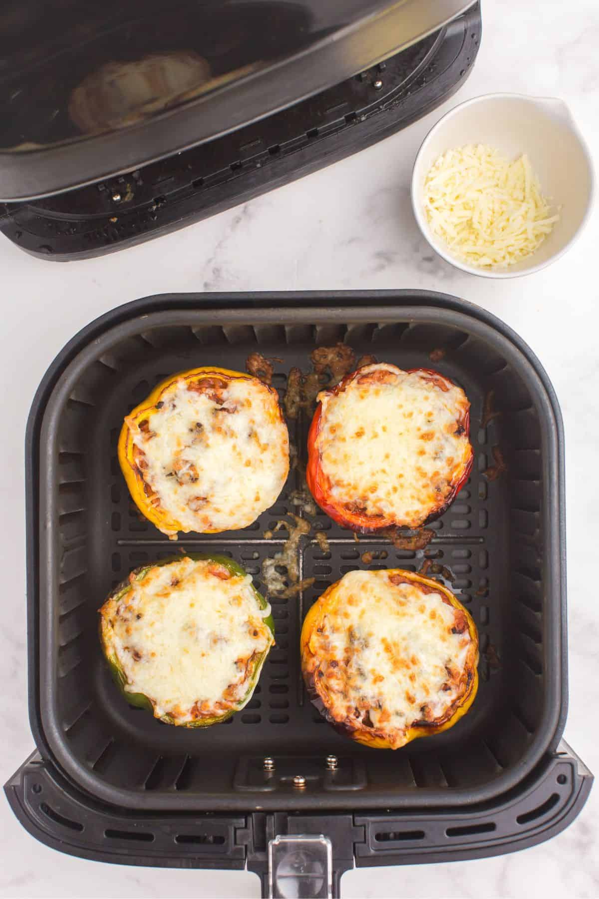 Cooked stuffed peppers in an air fryer basket with browned melted cheese on top.