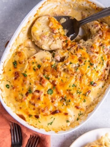 Instant pot scalloped potatoes and ham in a baking dish with a spoon in it.