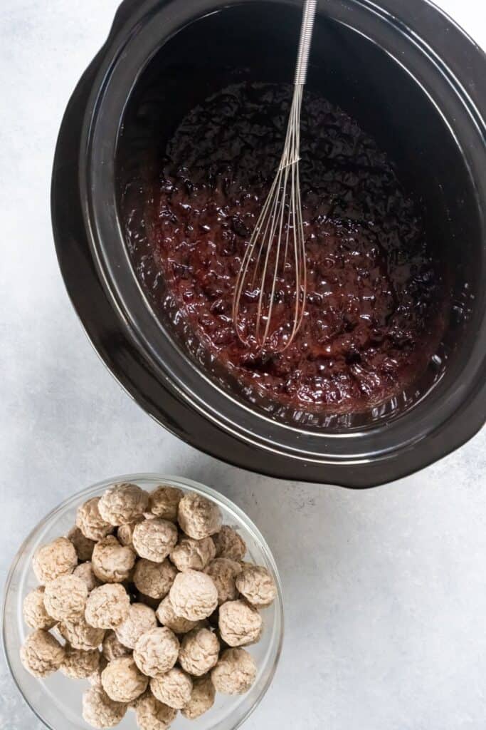 Grape jelly and cranberry sauce mixed in the slow cooker with frozen meatballs next to it.