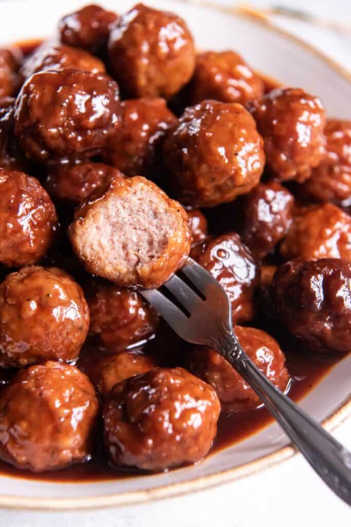 Slow cooker meatballs in a serving bowl with a bite taken out of one with a fork in it.