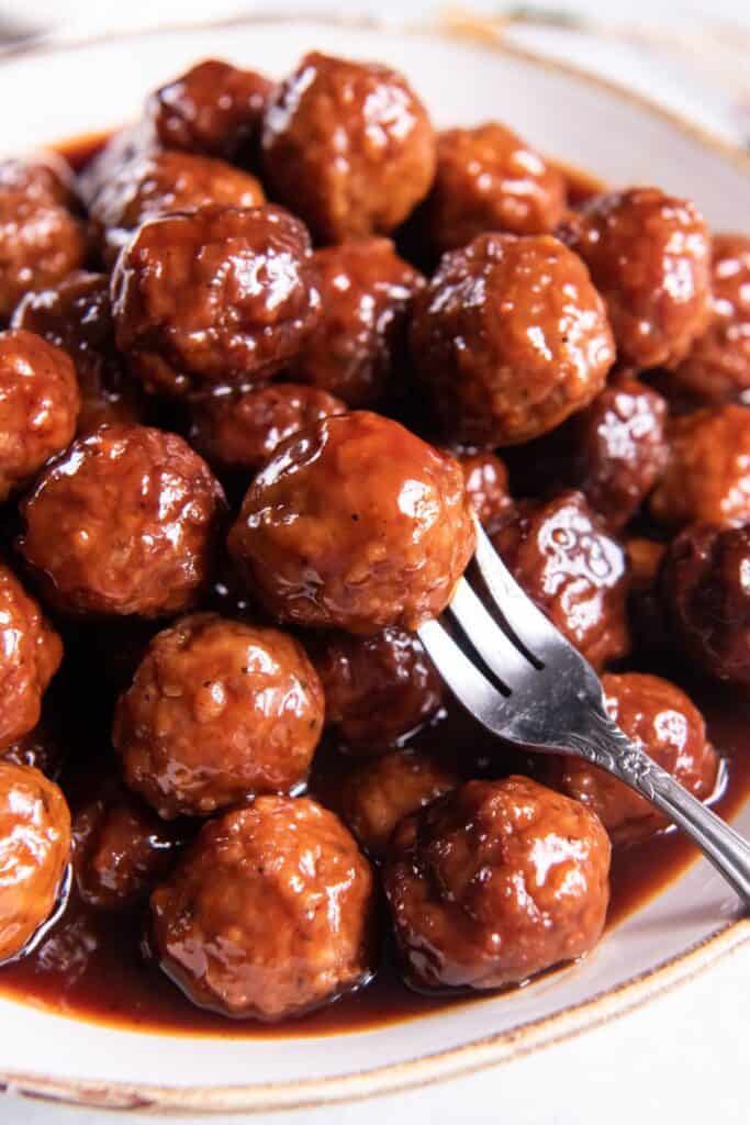 Meatballs with grape jelly and BBQ sauce in a serving bowl with a fork in one.