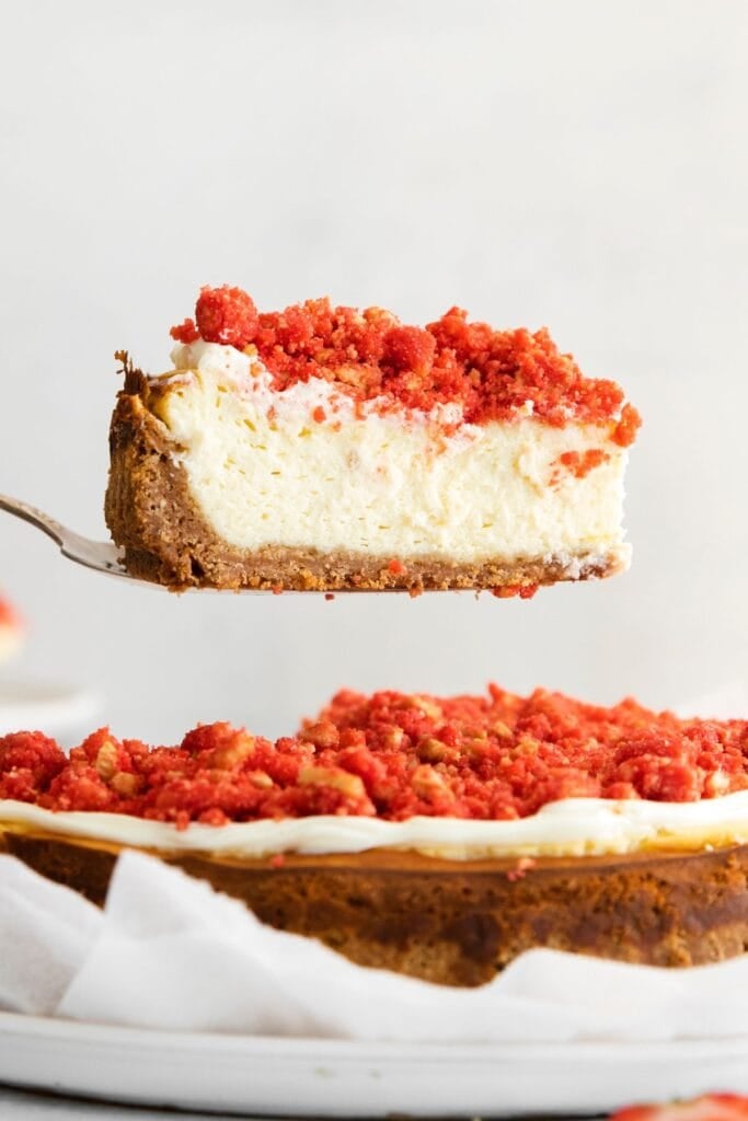 A slice of the strawberry crunch cheesecake being held up with a pie cutter so you can see the texture of inside the cheesecake.