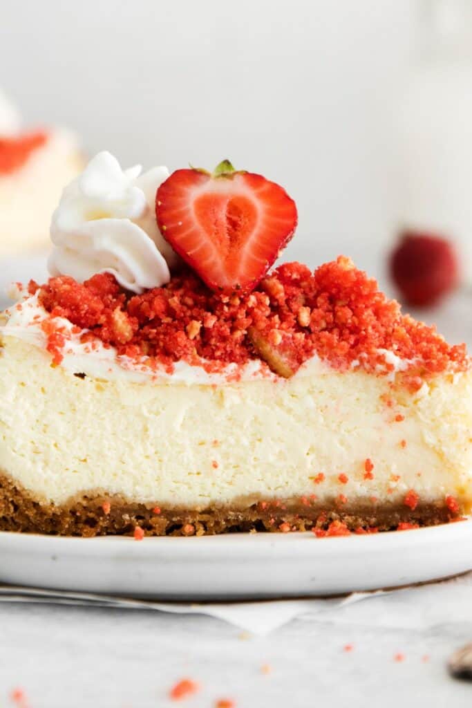 Strawberry crunch cheesecake slice with a strawberry and whipped cream on top close up from the side.