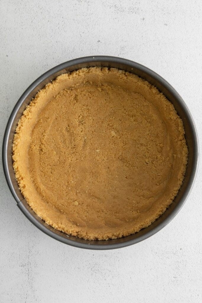 Graham cracker crust pressed into a spring form pan to make the berrylicious strawberry crunch cheesecake.