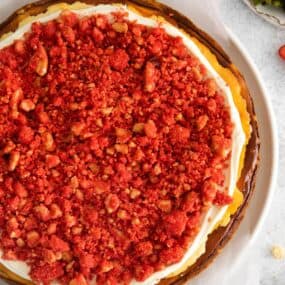 Finished strawberry cheesecake crunch cake recipe that's topped with the frosting and then the crunch topping.