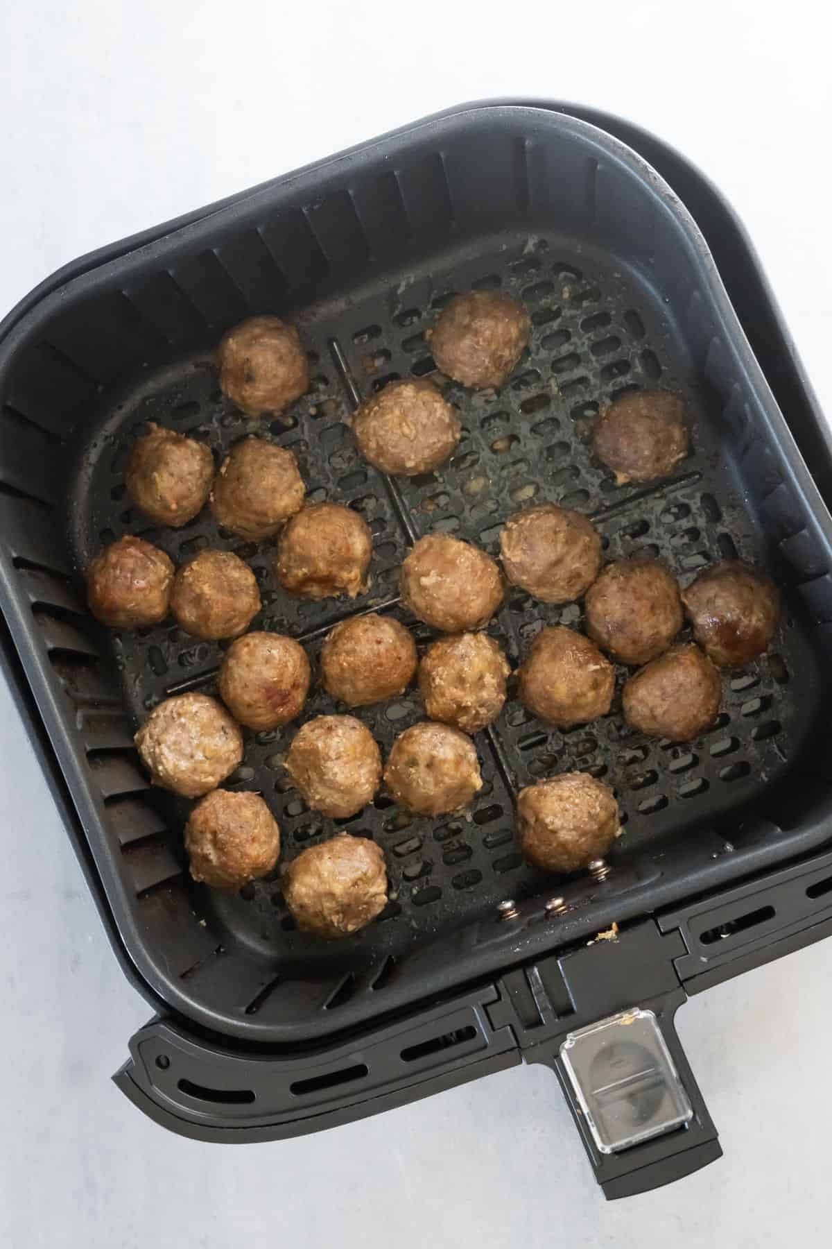 Cooked turkey meatballs in an air fryer basket.