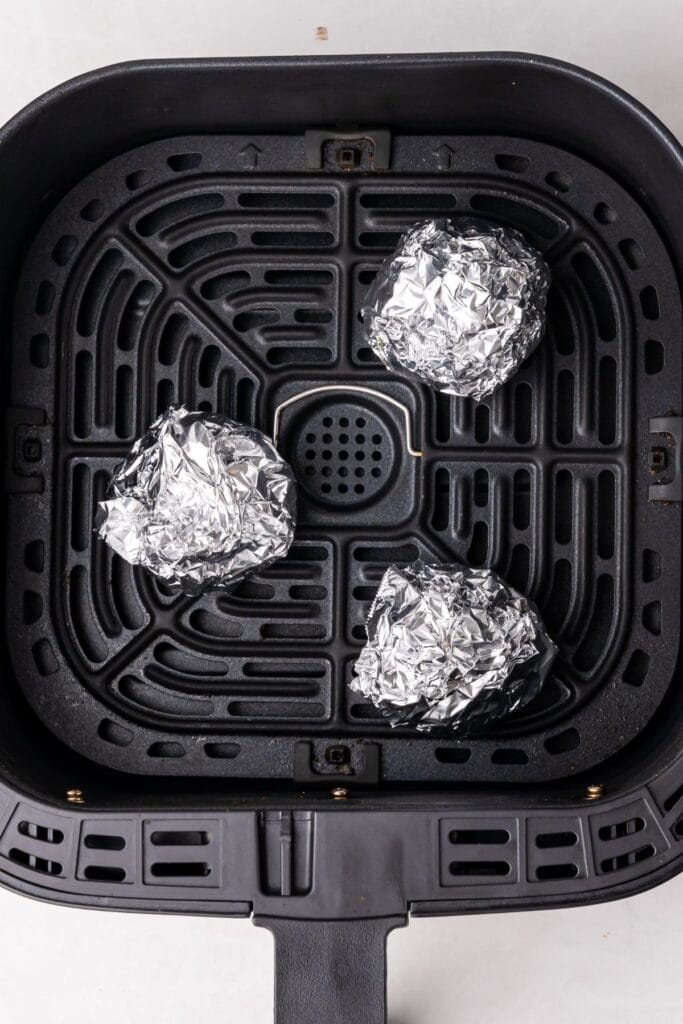 Roasted garlic in an air fryer basket wrapped in foil.