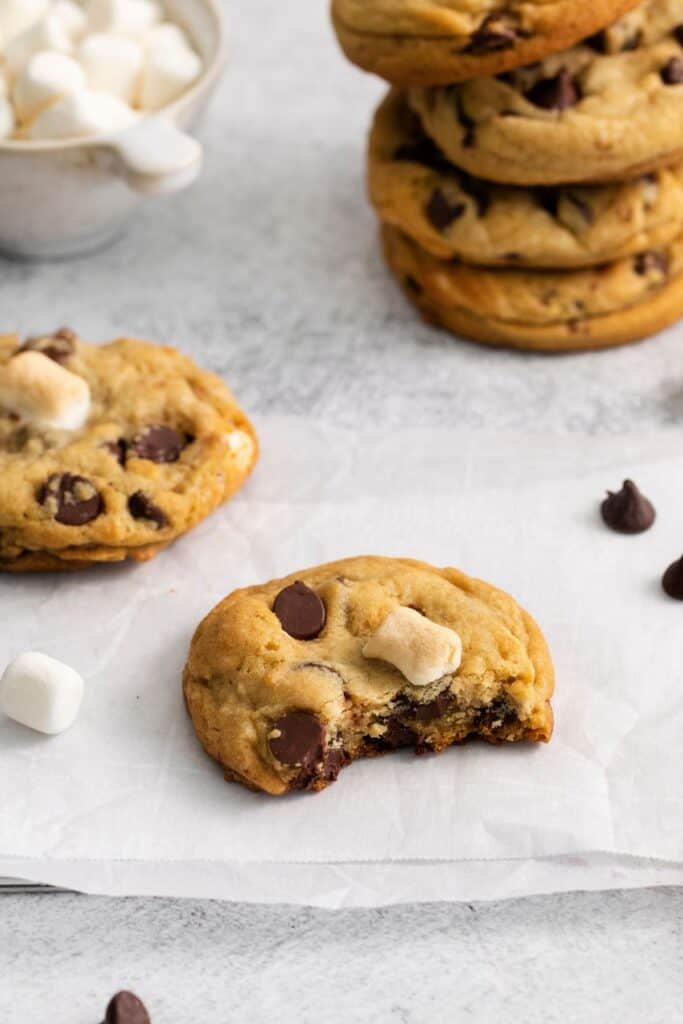 Marshmallow chocolate chip cookies on a counter with one of them with a bite taken out of it so you can see the inside.