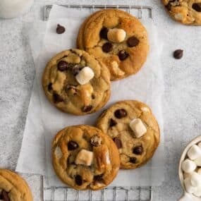 Chocolate chip marshmallow cookies on a counter with parchment paper and a wired rack.