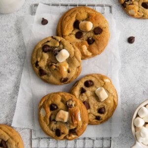Chocolate chip marshmallow cookies on a counter with parchment paper and a wired rack.