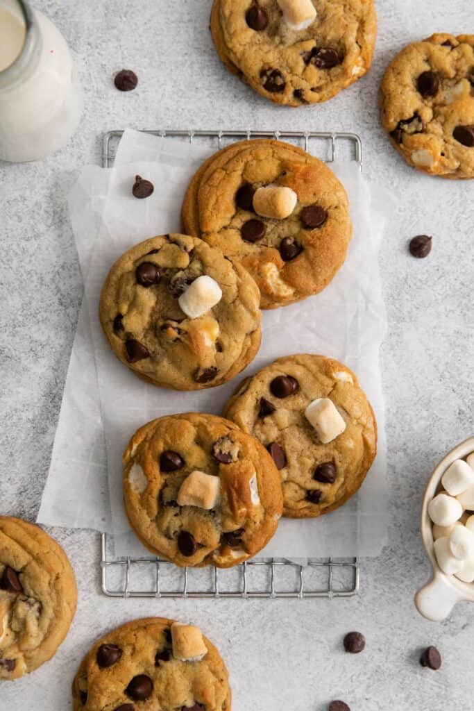 Chocolate chip marshmallow cookies on a counter with parchment paper and a wired rack.