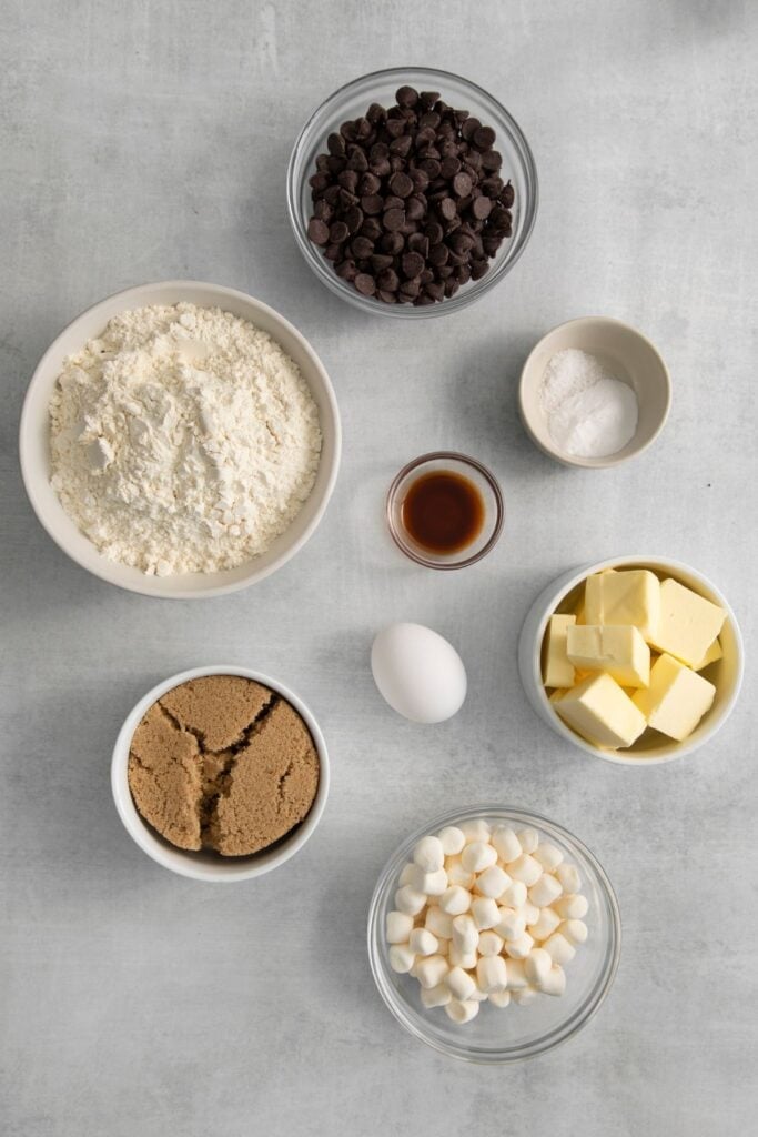 Ingredients needed to make chocolate chip marshmallow cookies: butter, brown sugar, egg, vanilla extract, flour, baking soda, chocolate chips, and marshmallows.