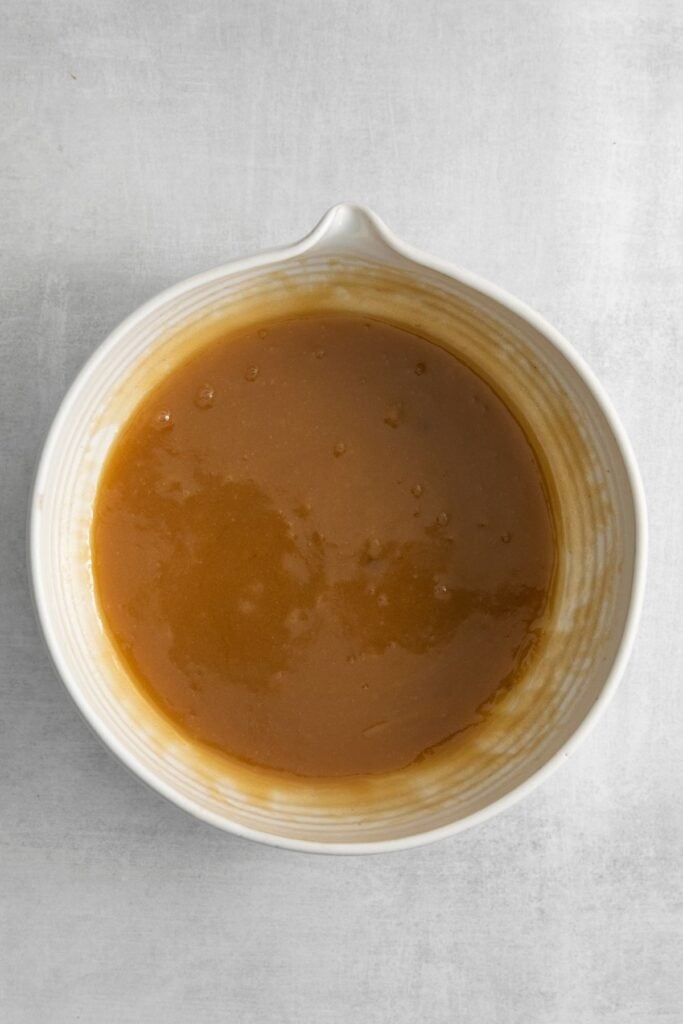 Mixing bowl with melted butter and brown sugar mixed together to make marshmallow chocolate chip cookies.