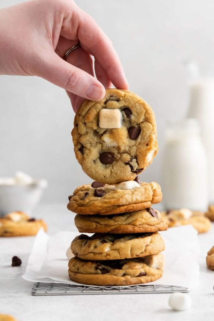 Marshmallow chocolate chip cookies stacked on top of each other with a hand holding up the top cookie.
