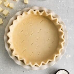 Easy pie crust recipe in a pie pan with the sides crimped and fork holes on the bottom about to be baked.