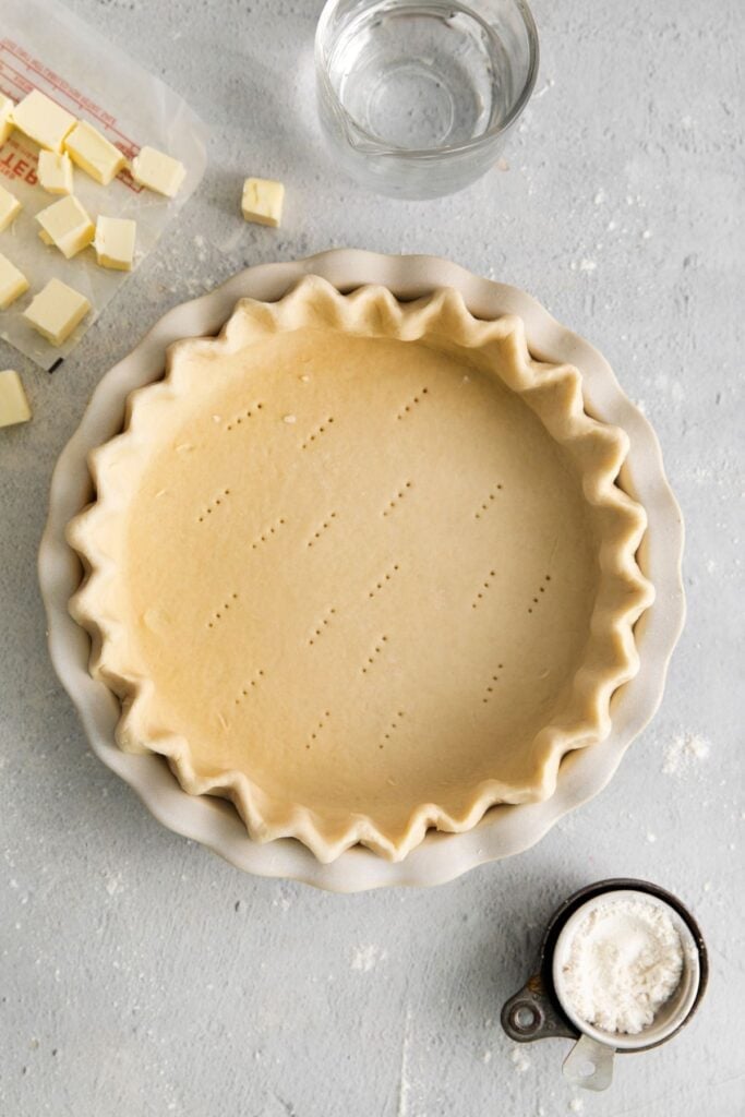 Easy pie crust recipe in a pie pan with the sides crimped and fork holes on the bottom about to be baked.