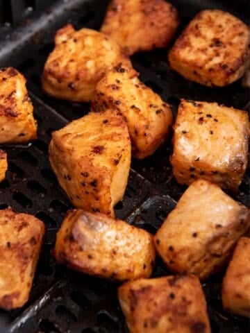 Close up of air fryer salmon bites in an air fryer basket.