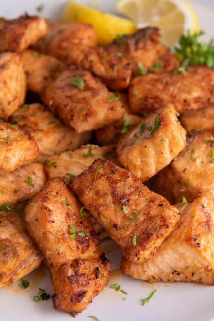 air fryer salmon bites on a white plate next to a lemon wedge.