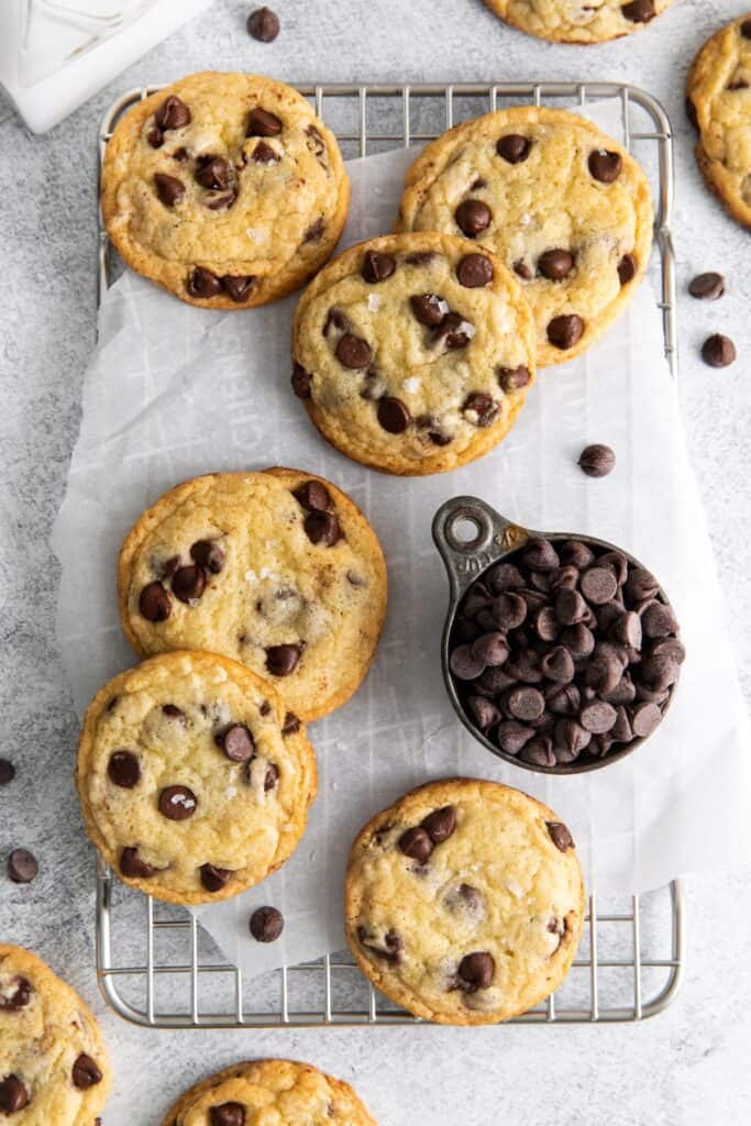 Chocolate chip cookie recipe without brown sugar on a wire rack with some parchment paper and a small bowl of chocolate chips.