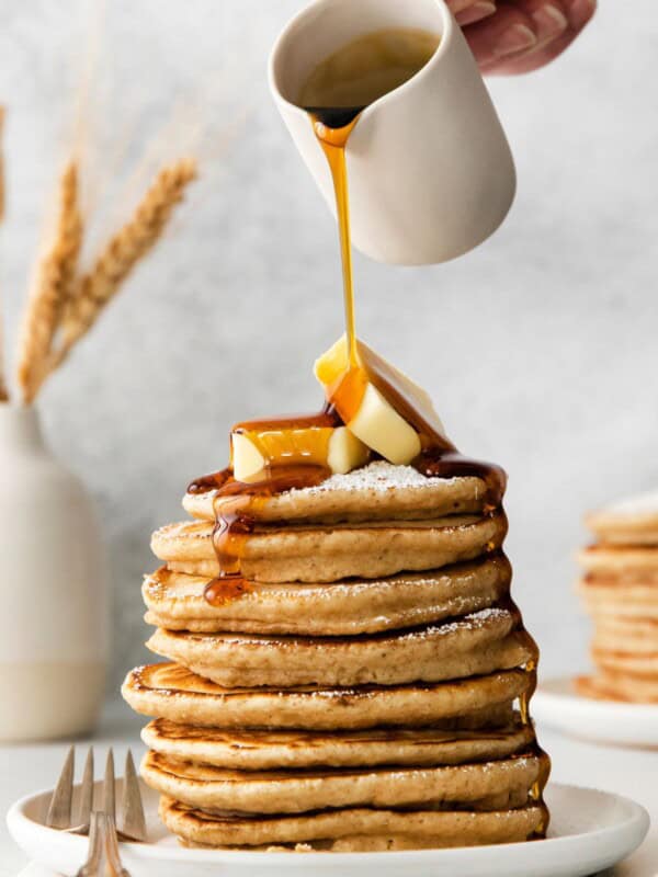 French toast pancakes stacked on a plate with butter on top and maple syrup being poured over top.