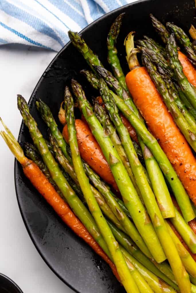 Roasted carrots and asparagus on a black serving plate.