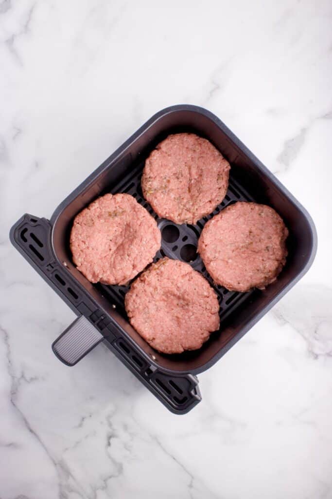 Raw hamburgers in an air fryer basket.