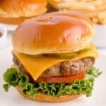 Air fryer hamburger on a white plate with a bun, cheese, lettuce, tomato, and pickles.