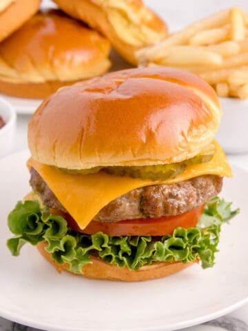 Air fryer hamburger on a white plate with a bun, cheese, lettuce, tomato, and pickles.