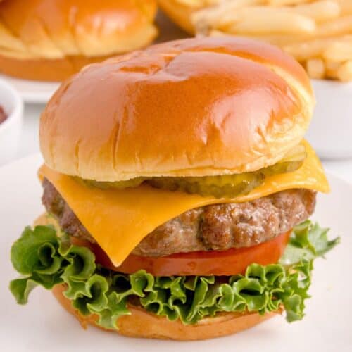 Air fryer hamburger on a white plate with a bun, cheese, lettuce, tomato, and pickles.