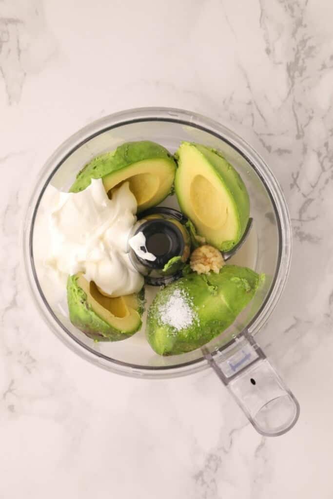 Avocado halves and other ingredients in food processor from overhead