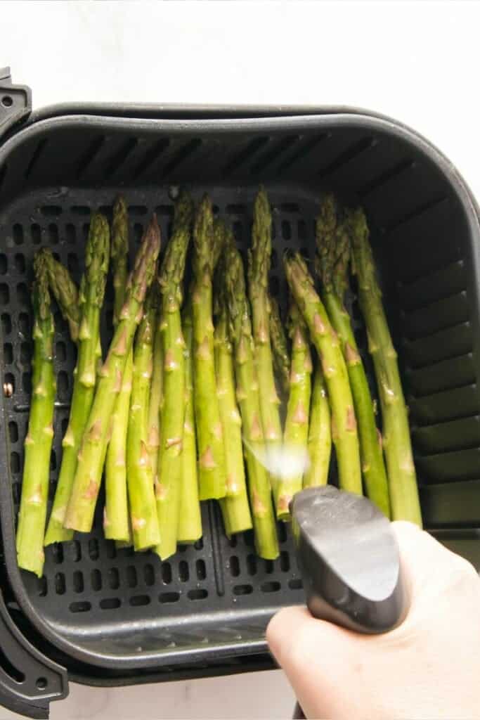 Asparagus being sprayed with oil in air fryer basket