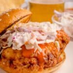 Buffalo chicken sandwich with coleslaw on top with the bun half on.