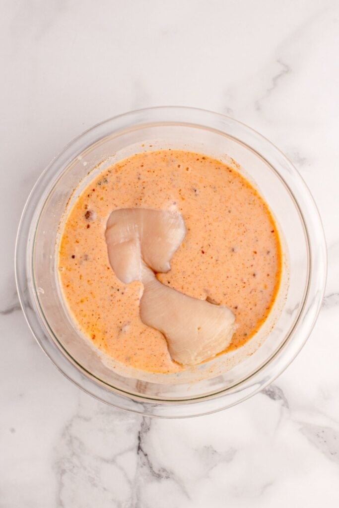 Buffalo chicken being marinaded in buffalo mixture in a mixing bowl.
