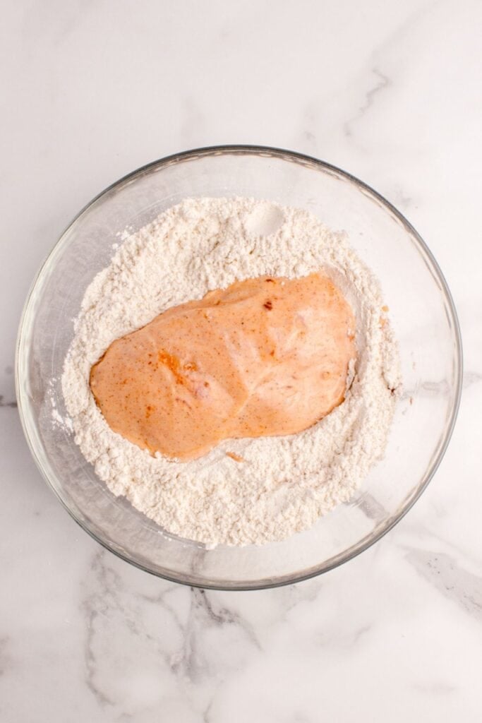 Buffalo coated chicken being dipped in the flour to get a nice crispy coating on it when fried.