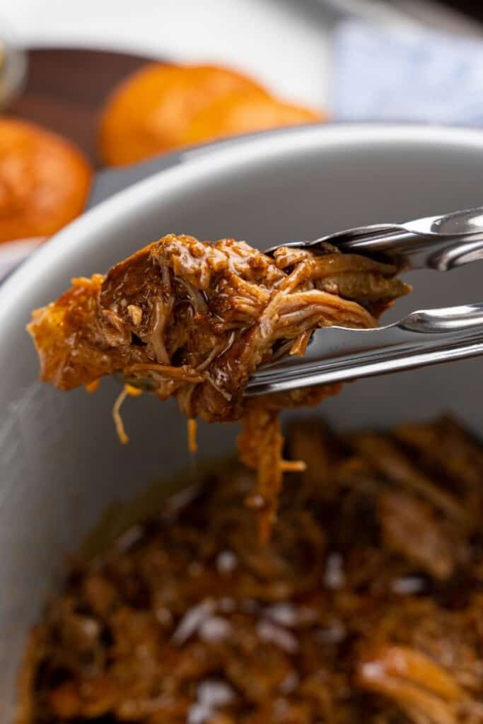 tongs holding juicy shredded pork