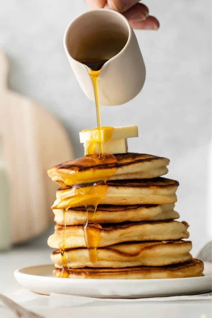 pouring syrup over stack of pancakes