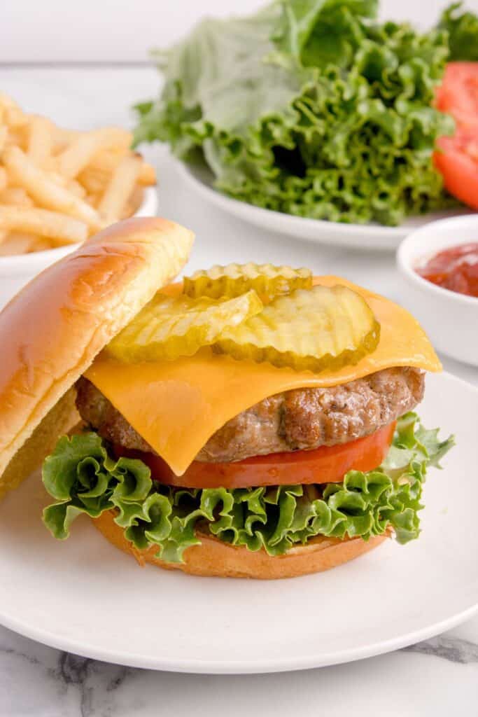 Air fryer hamburger on a plate with a bun off to the side so you can see the pickles and cheese on top.