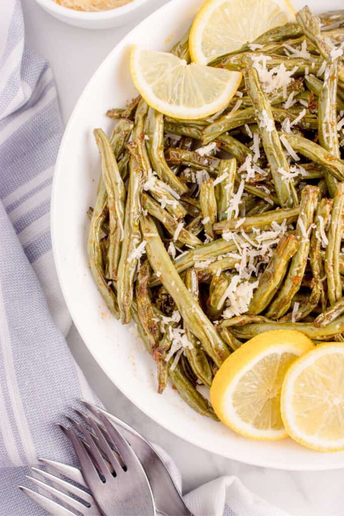 Plated air fried green beans served with Parmesan cheese and lemon slices.
