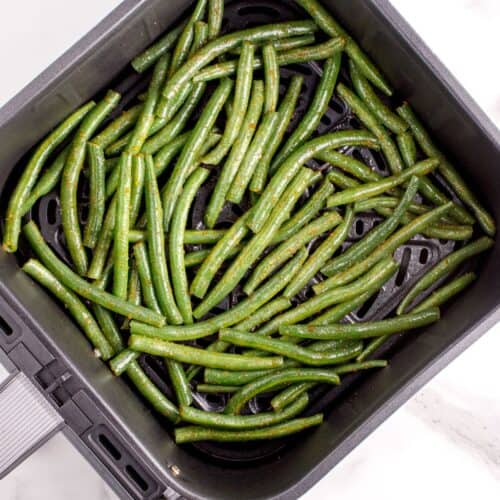 Raw fresh green beans in the air fryer basket about to be air fried.