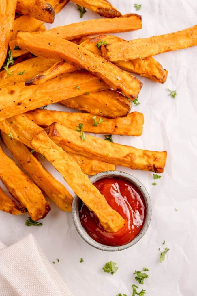 Air fryer sweet potato fries with one fry being dipped into a small bowl of ketchup.