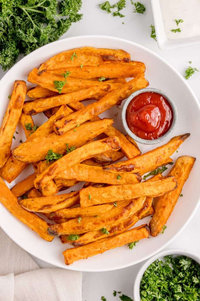 Overhead shot of air fryer sweet potato fries on a white plate served with ketchup.