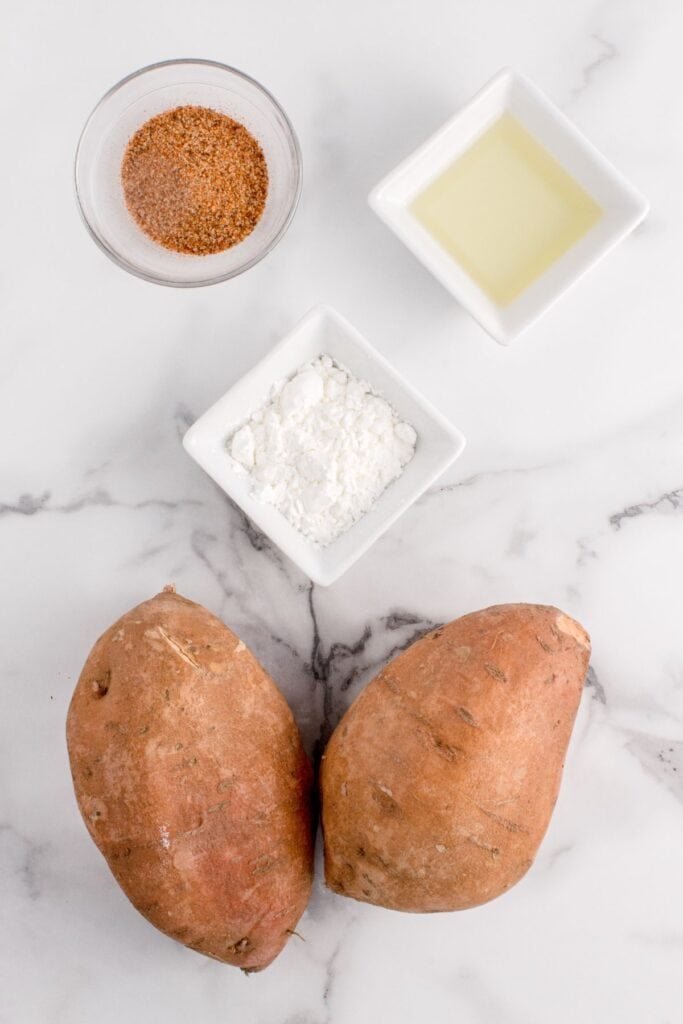Ingredients needed to air fry sweet potato fries: sweet potatoes, cornstarch, olive oil, and Cajun seasoning.