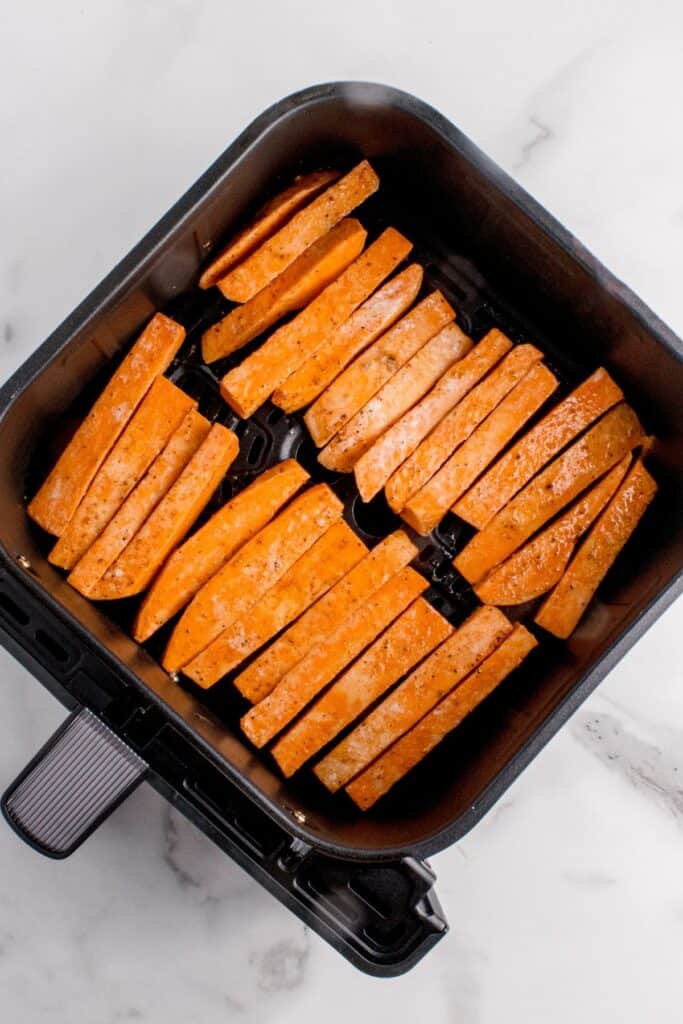 Raw sweet potato fries in an air fryer basket ready to be air fried.