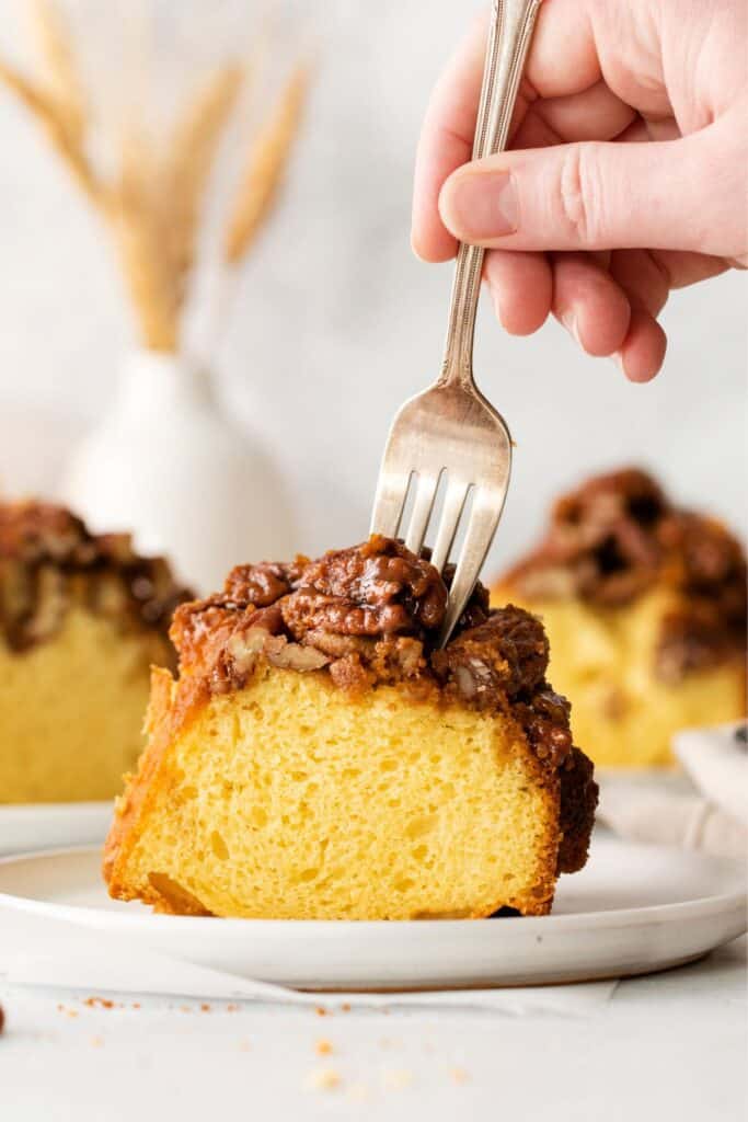A fork taking a piece of the pecan pie upside down cake slice on a plate.